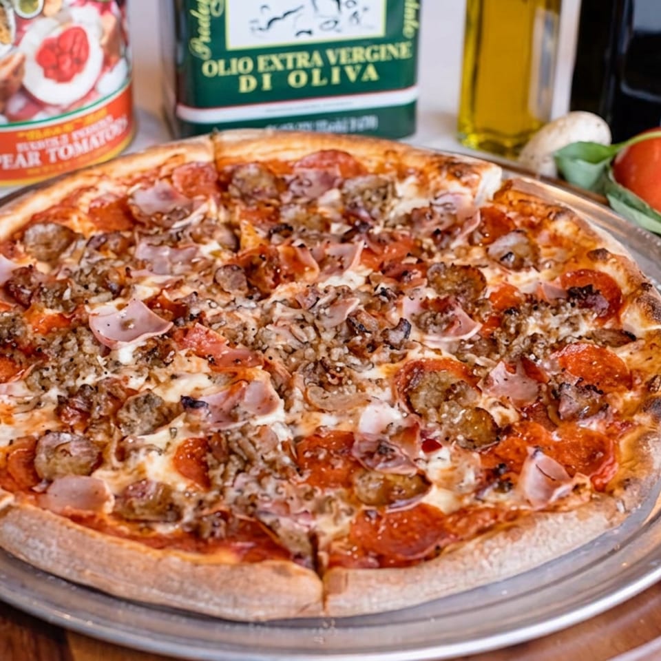 Large meat-lovers pizza topped with pepperoni, sausage, ham, mushrooms, and cheese on a metal serving tray with Italian ingredients.