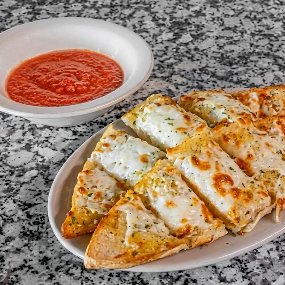 Plate of cheesy garlic bread slices served with marinara dipping sauce on a granite countertop.