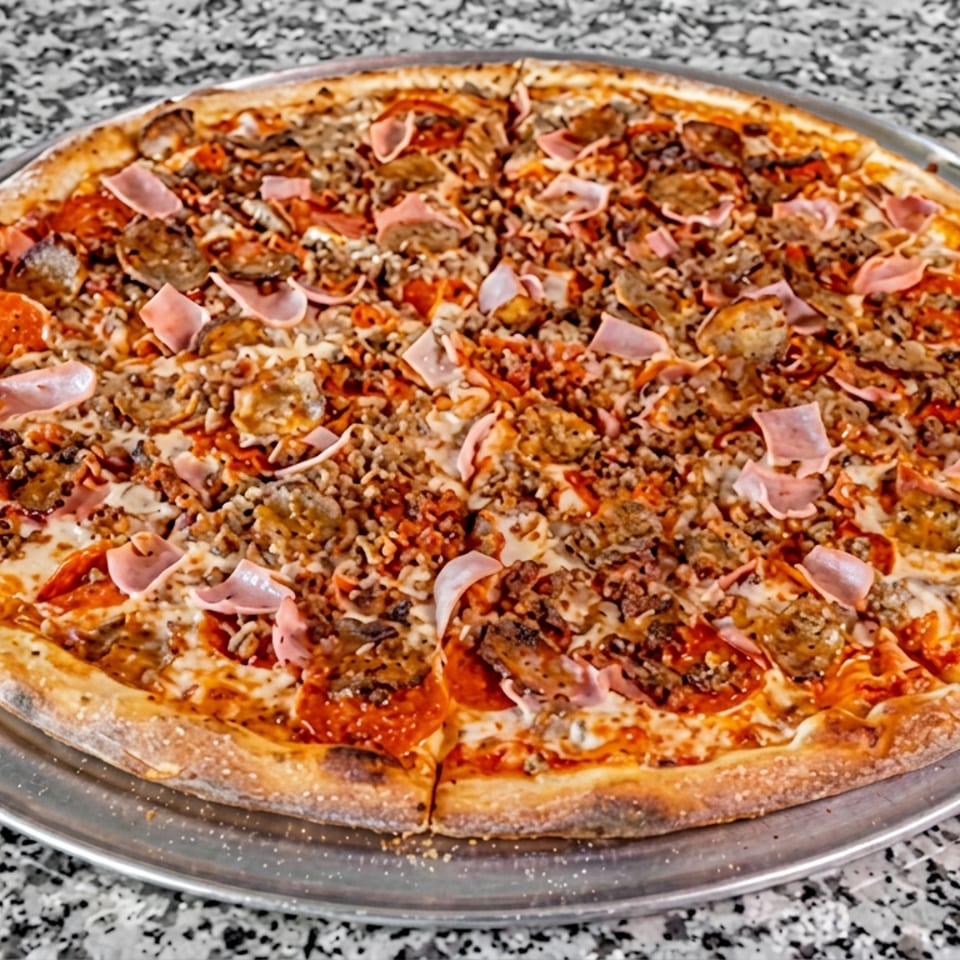 Large loaded meat-lovers pizza with pepperoni, sausage, ground meat, ham, mushrooms, and melted cheese on a metal tray.