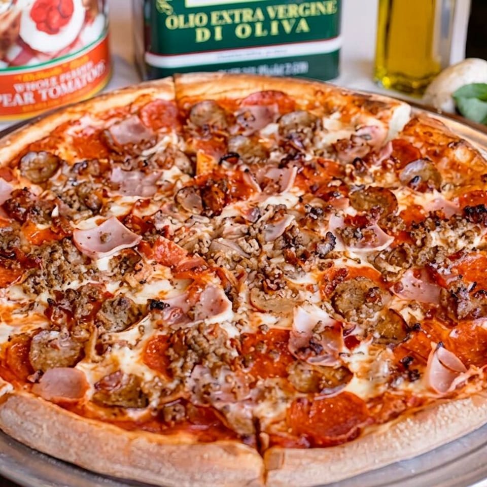 Loaded pizza topped with pepperoni, sausage, ground meat, ham, mushrooms, and melted cheese on a metal tray.
