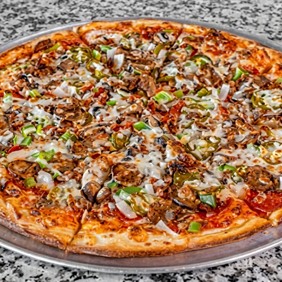 Large loaded pizza topped with mushrooms, green peppers, onions, olives, sausage, and melted cheese on a metal tray.